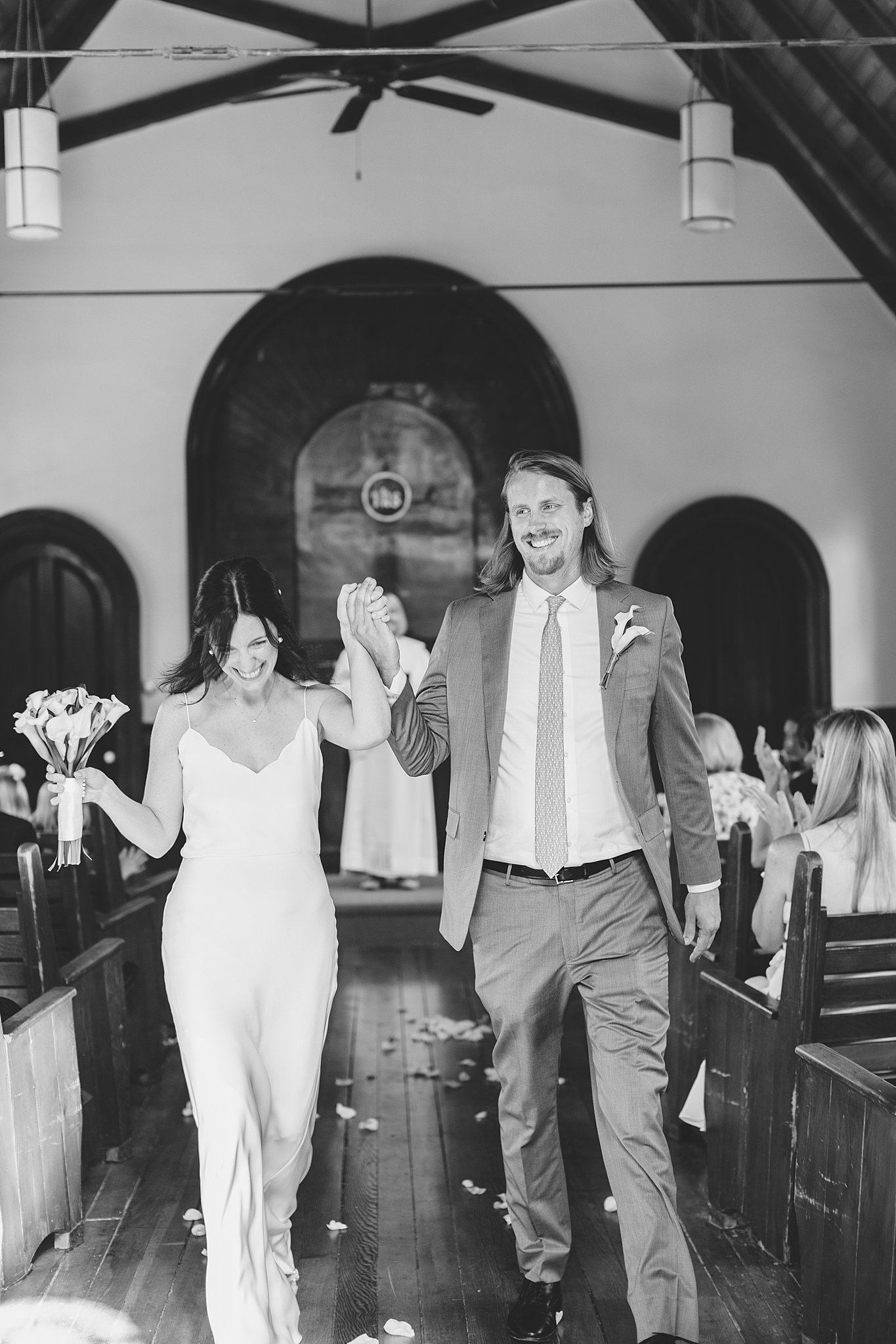 Happy newlyweds hold hands while smiling and exiting their fort sherman chapel wedding ceremony