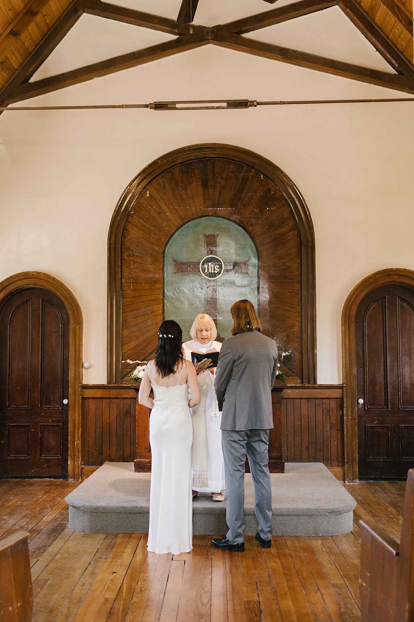 A bride and groom stand at the altar facing their officiant as she reads at the fort sherman chapel