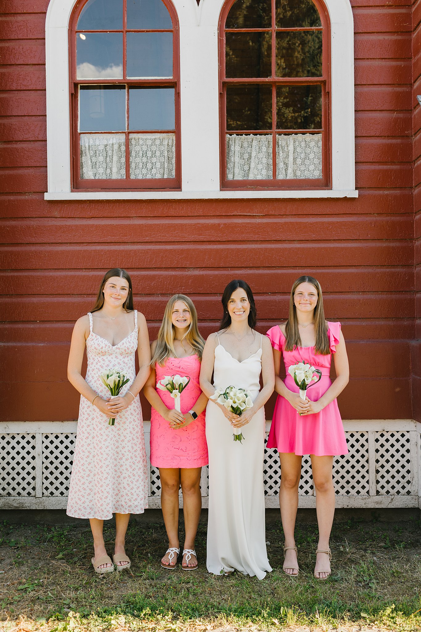 A bride stands with her bridesmaids outside the chapel holding matching white bouquets