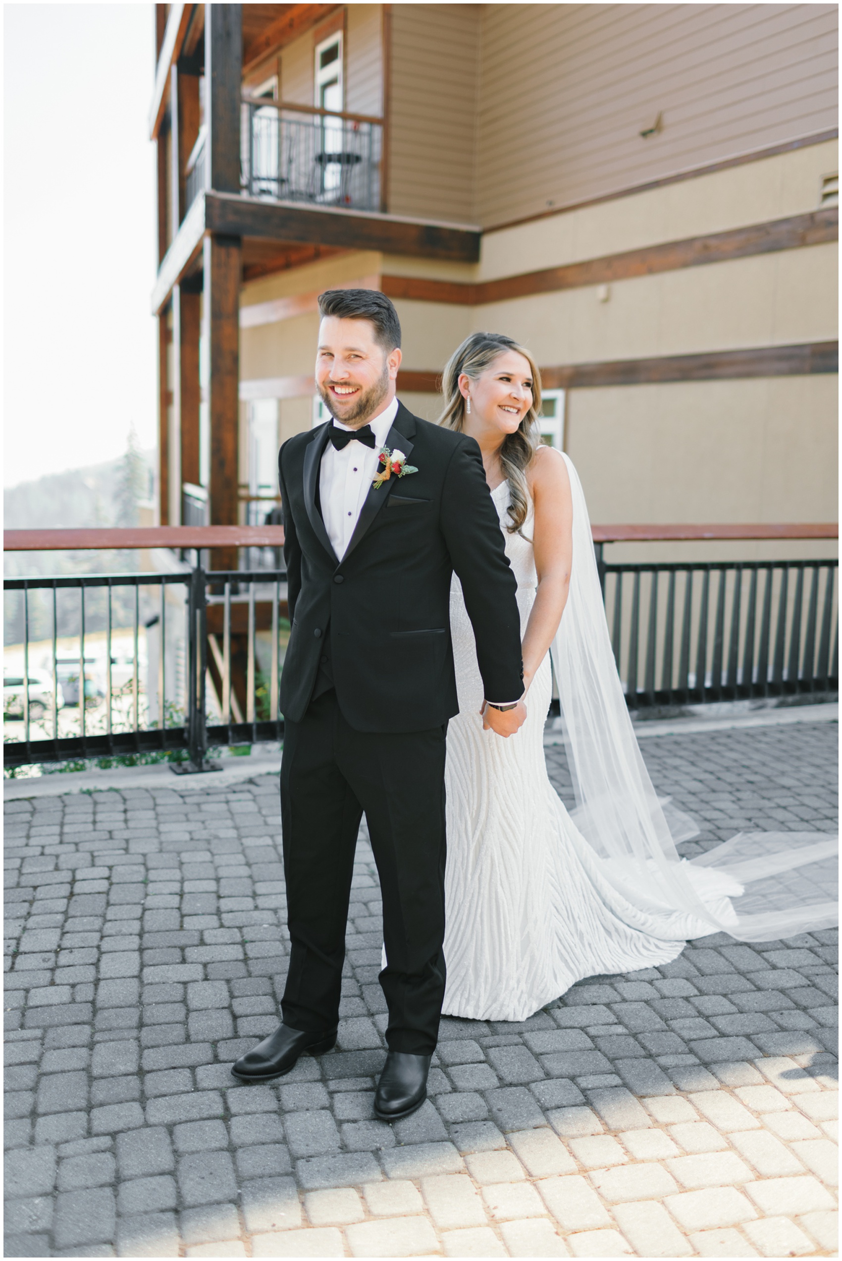 A groom holds hands behind his back with his bride on a patio