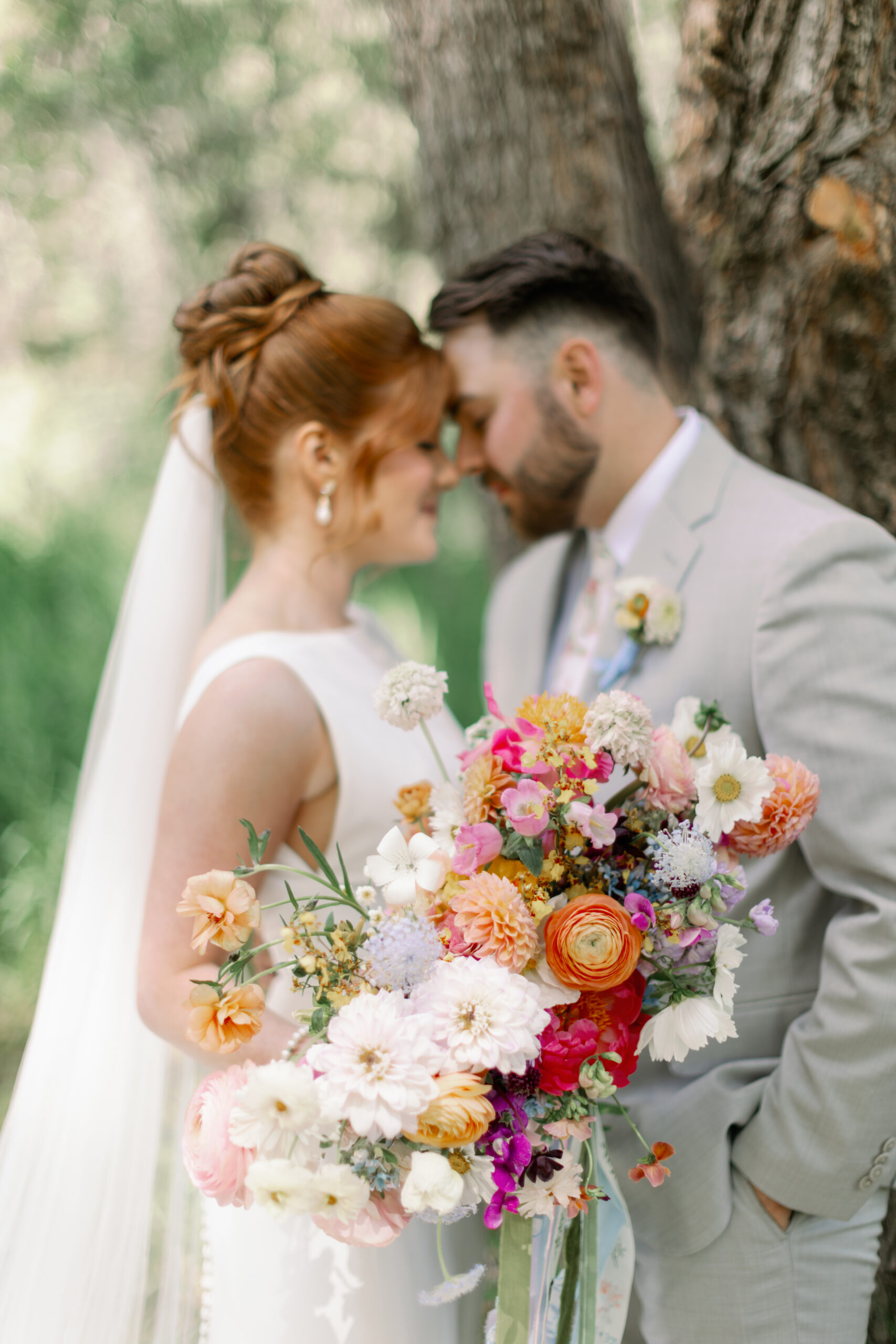 A wedding couple with a colorful bridal bouquet is standing face to face tenderly