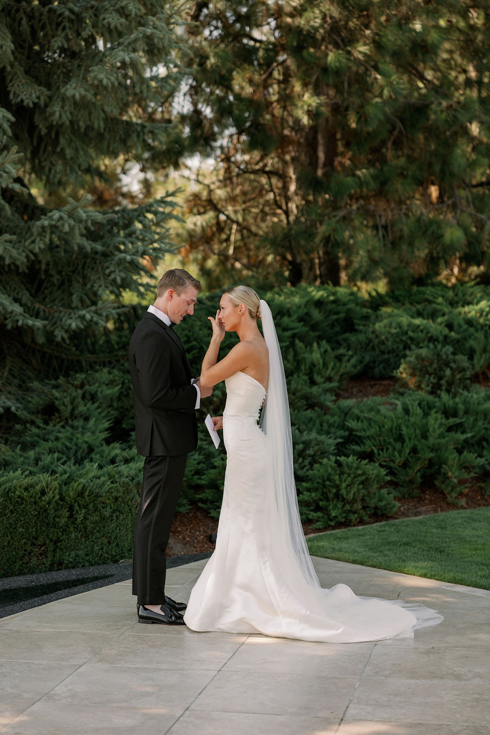 A bride cries and wipes away tears during her first look and note readings in a garden